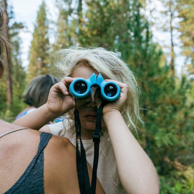 A child in their parent's arms peers through bright blue binoculars. Photo: Sean Rea.